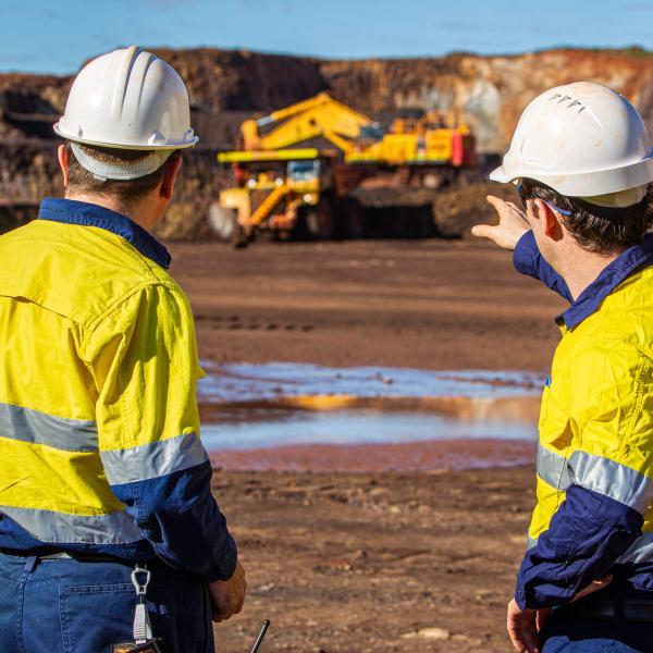 Two people on a red dirt looking at a truck